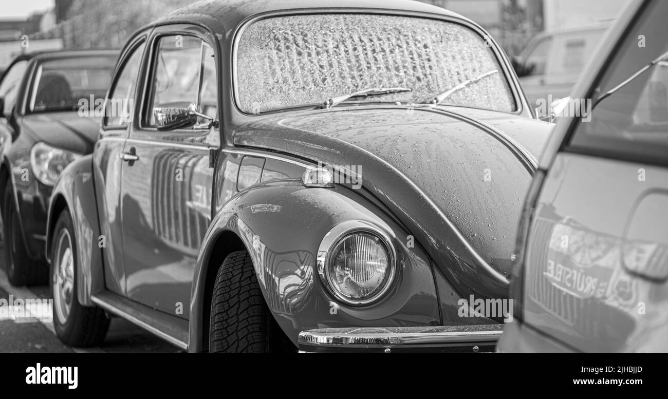 A panoramic black and white shot of parked old classic car Volkswagen Beetle in the street Stock Photo