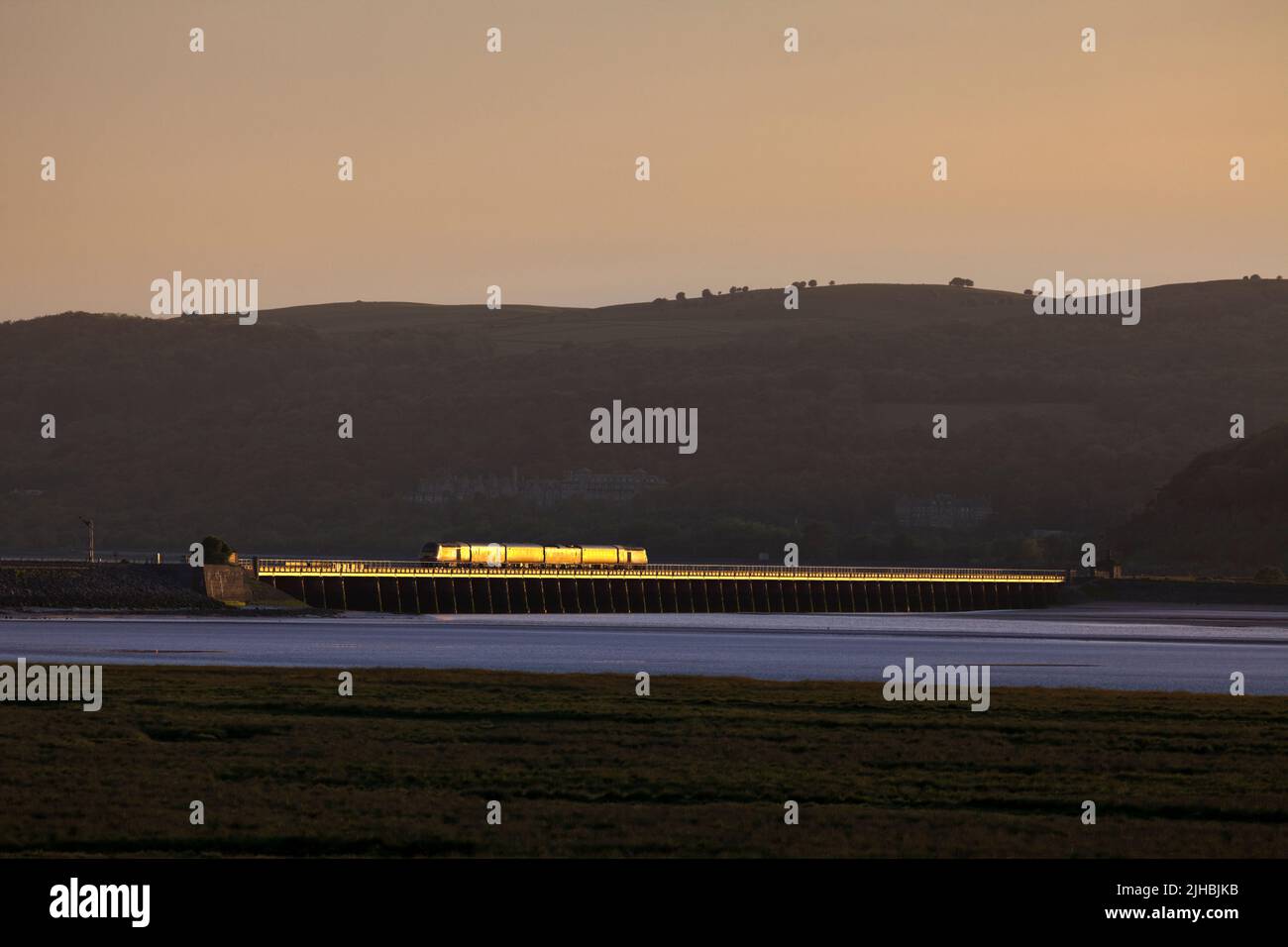 Network Rail Infrastructure monitoring train crossing Arnside viaduct on the scenic Cumbrian Coast railway line with a gold glint at sunset Stock Photo