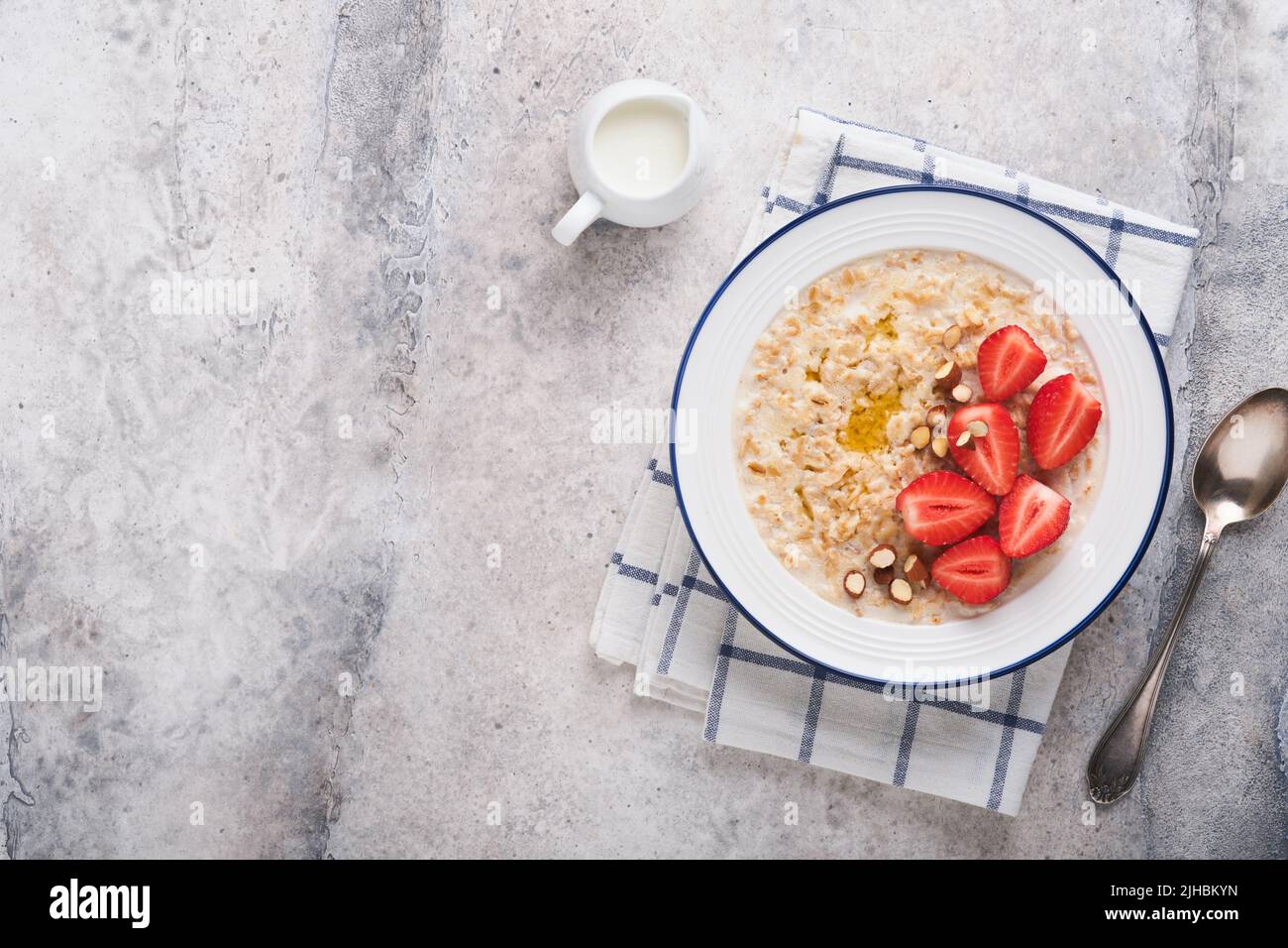 Oatmeal. Bowl of oatmeal porridge with strawberry, almond and milk on vintage light grey teal table. Top view in flat lay style. Natural ingredients. Stock Photo