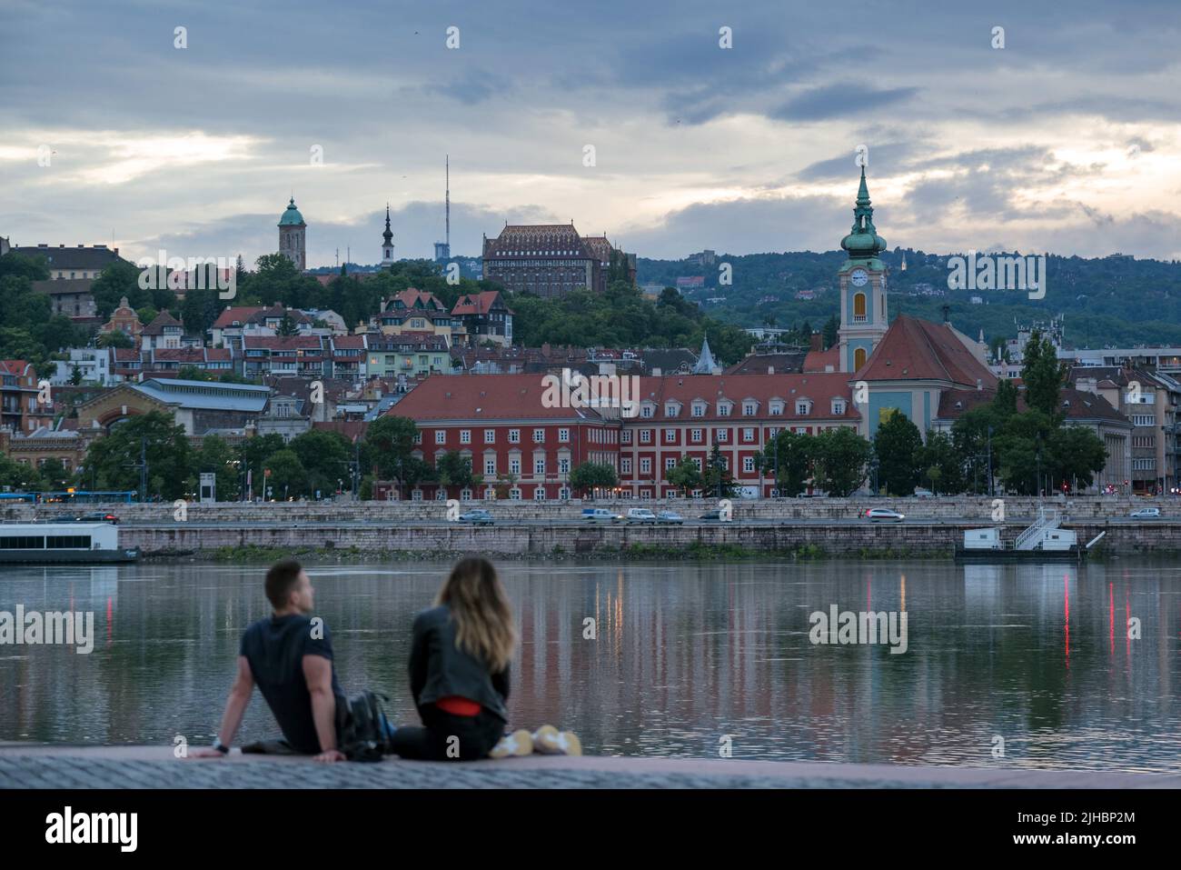 Unfocused relaxed couple sitting by the river against old city in dusk Stock Photo