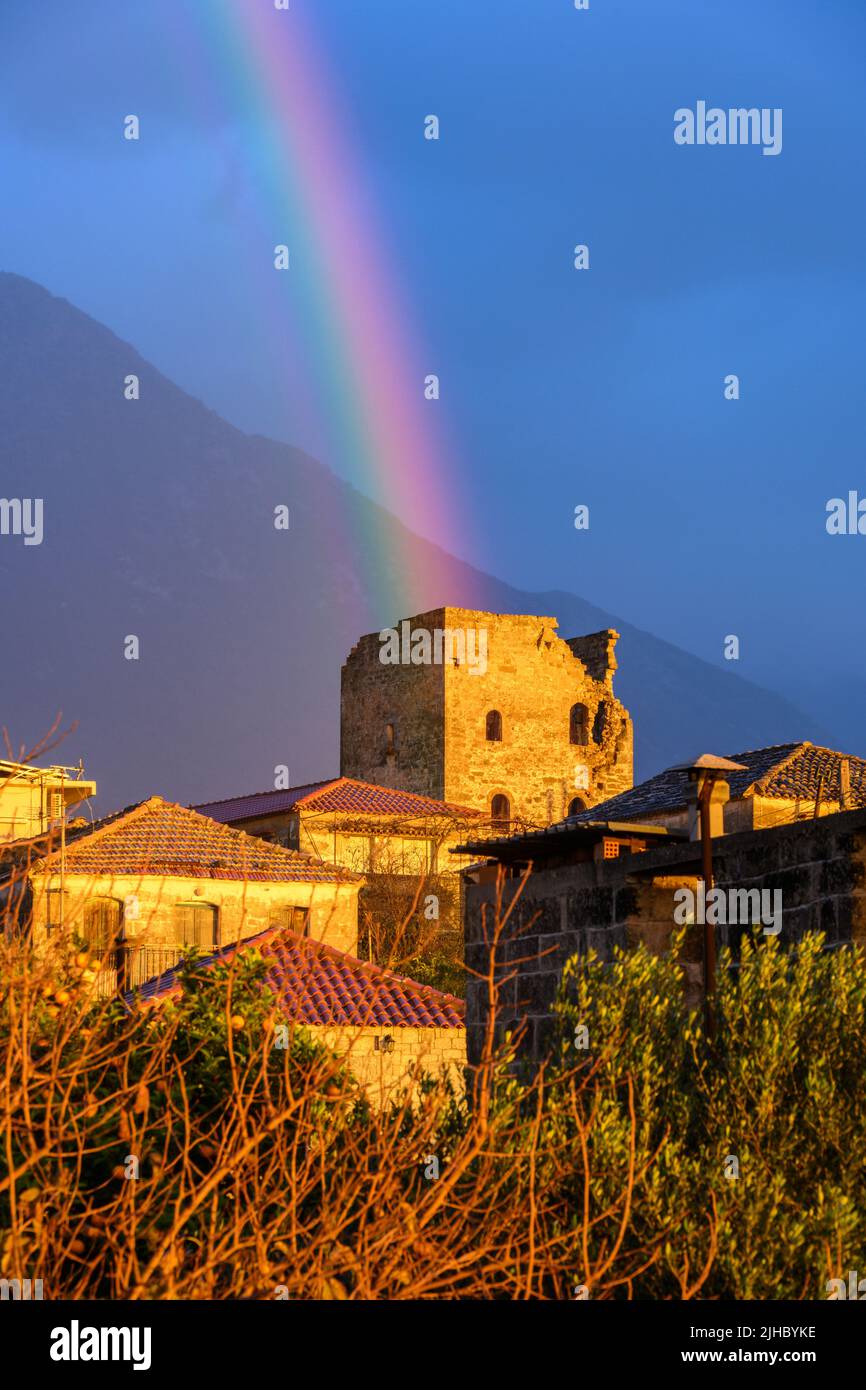 A rainbow appears behind an old Mani tower after a shower at sunset in the village of Proastio, Outer Mani, Messinia, Peloponnese, Greece. Stock Photo