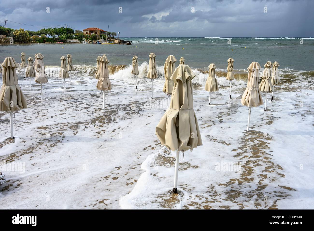 A late season storm causes waves to inundate the beach and beach umbrellas at the little resort of Stoupa in the Outer Mani, Messinia, Peloponnese, Gr Stock Photo