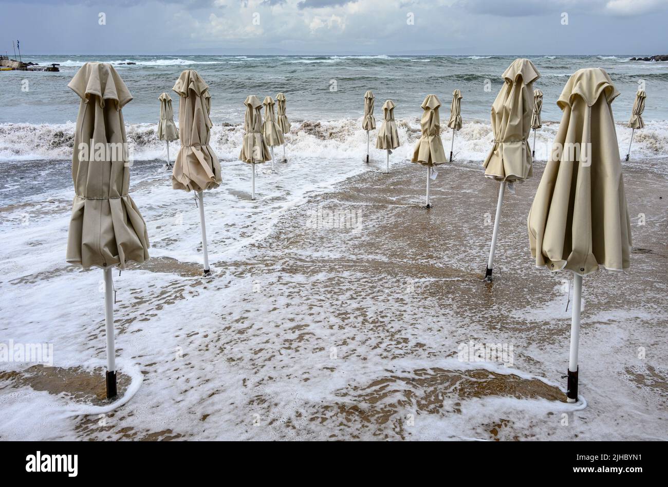 A late season storm causes waves to inundate the beach and beach umbrellas at the little resort of Stoupa in the Outer Mani, Messinia, Peloponnese, Gr Stock Photo