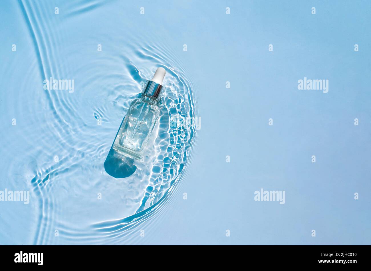 Moisturizing cosmetic product, serum in a transparent bottle with a dropper in water waves, blue background. Cosmetic and spa concept, copy space Stock Photo