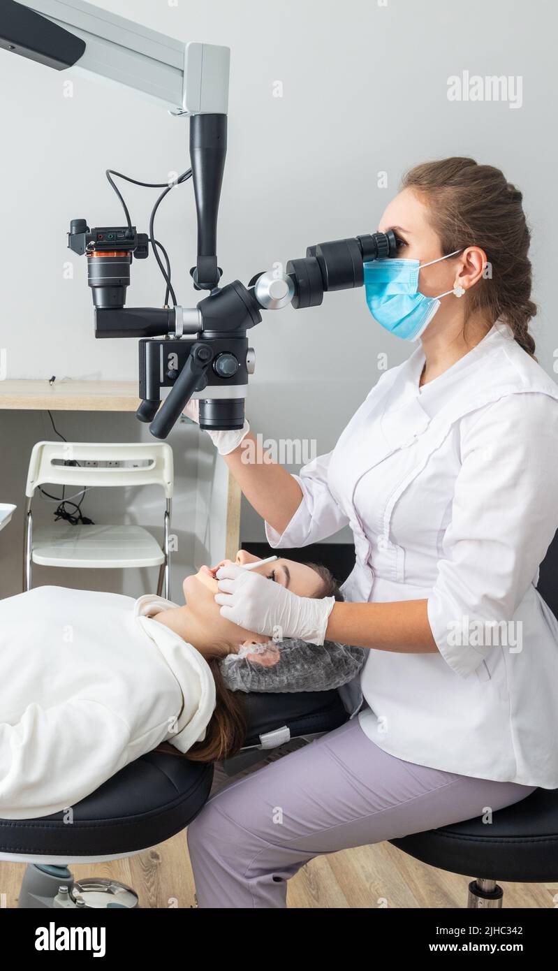 Female dentist using dental microscope treating patient teeth at dental