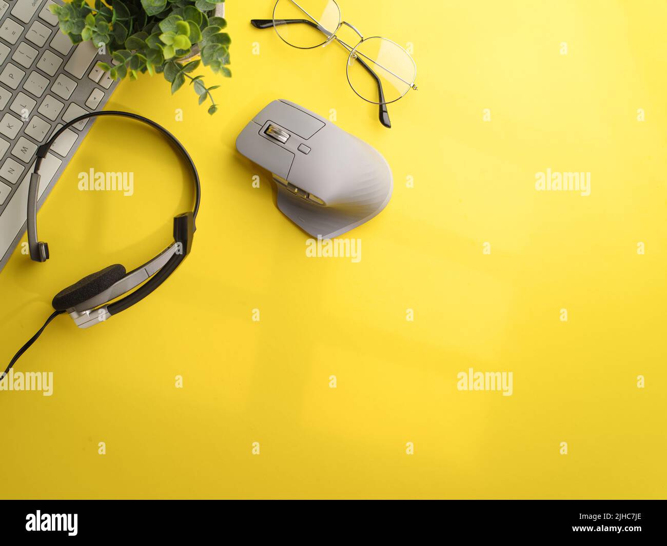 On a bright yellow background, a laptop, headphones, a computer mouse and a room flower decor. Modern workplace of a student, journalist, businessman. Stock Photo