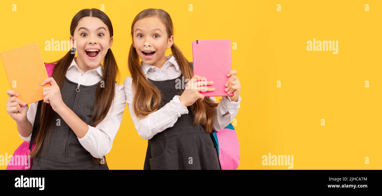 School girls friends. Read me story. Surprised kids hold books yellow background. Childrens literature. Portrait of schoolgirl student, studio banner Stock Photo