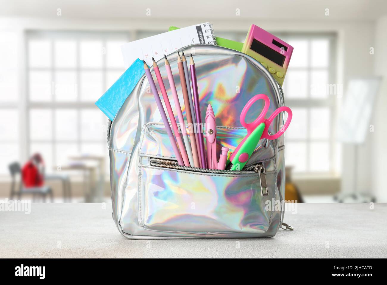 School backpack with stationery on table in classroom Stock Photo