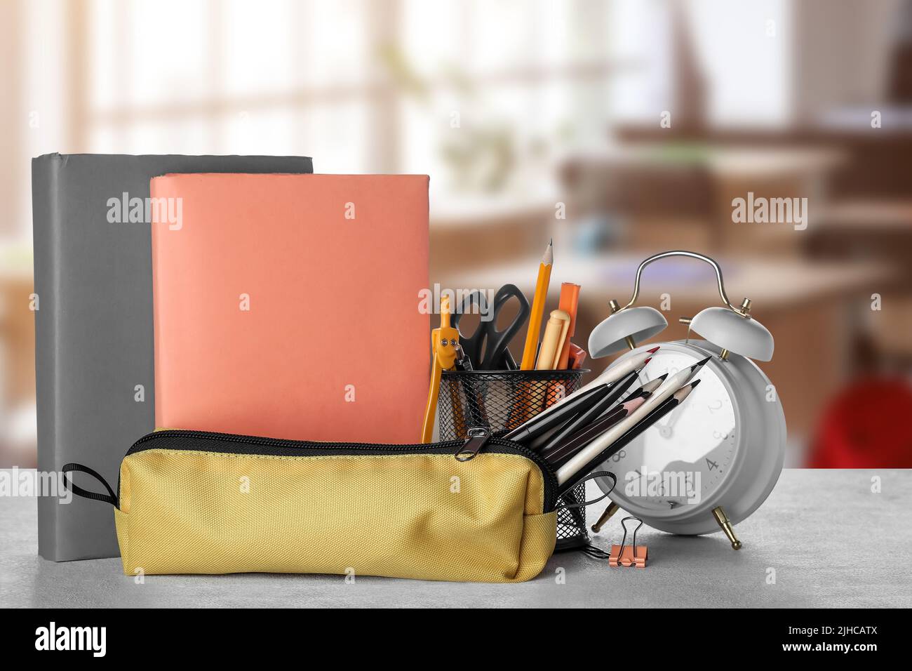 Set of school supplies and clock on table in classroom Stock Photo