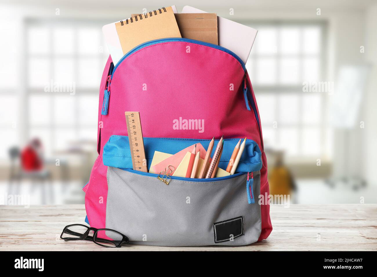 School backpack with stationery on table in classroom Stock Photo