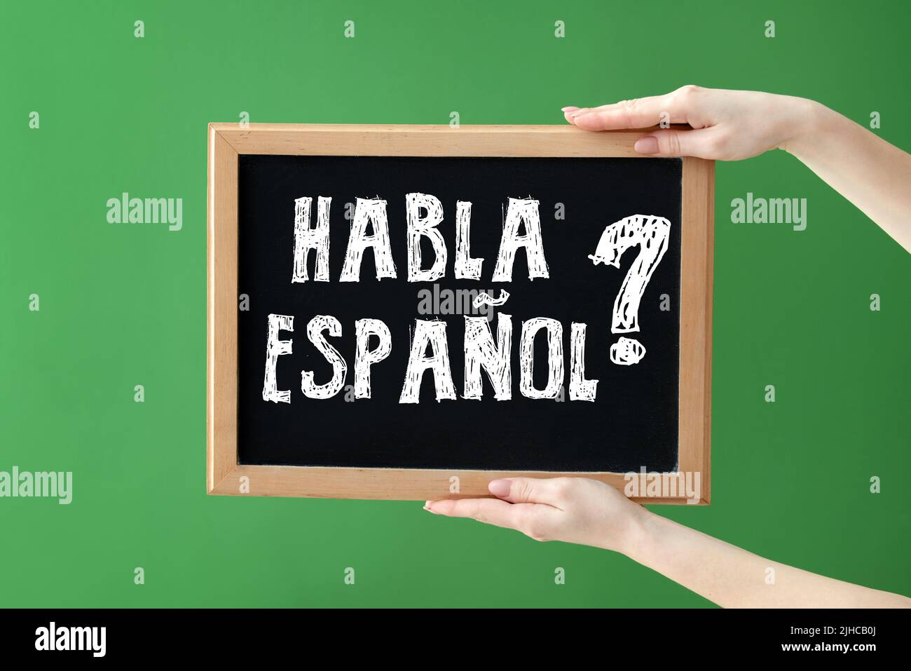 Hands holding chalkboard with text HABLA ESPANOL? (DO YOU SPEAK SPANISH?) on green background