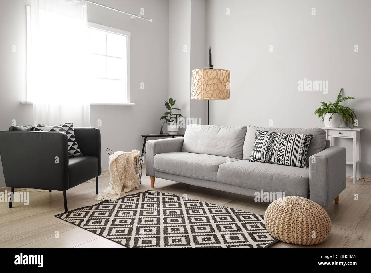 Interior of light living room with grey sofa, tables and armchair Stock
