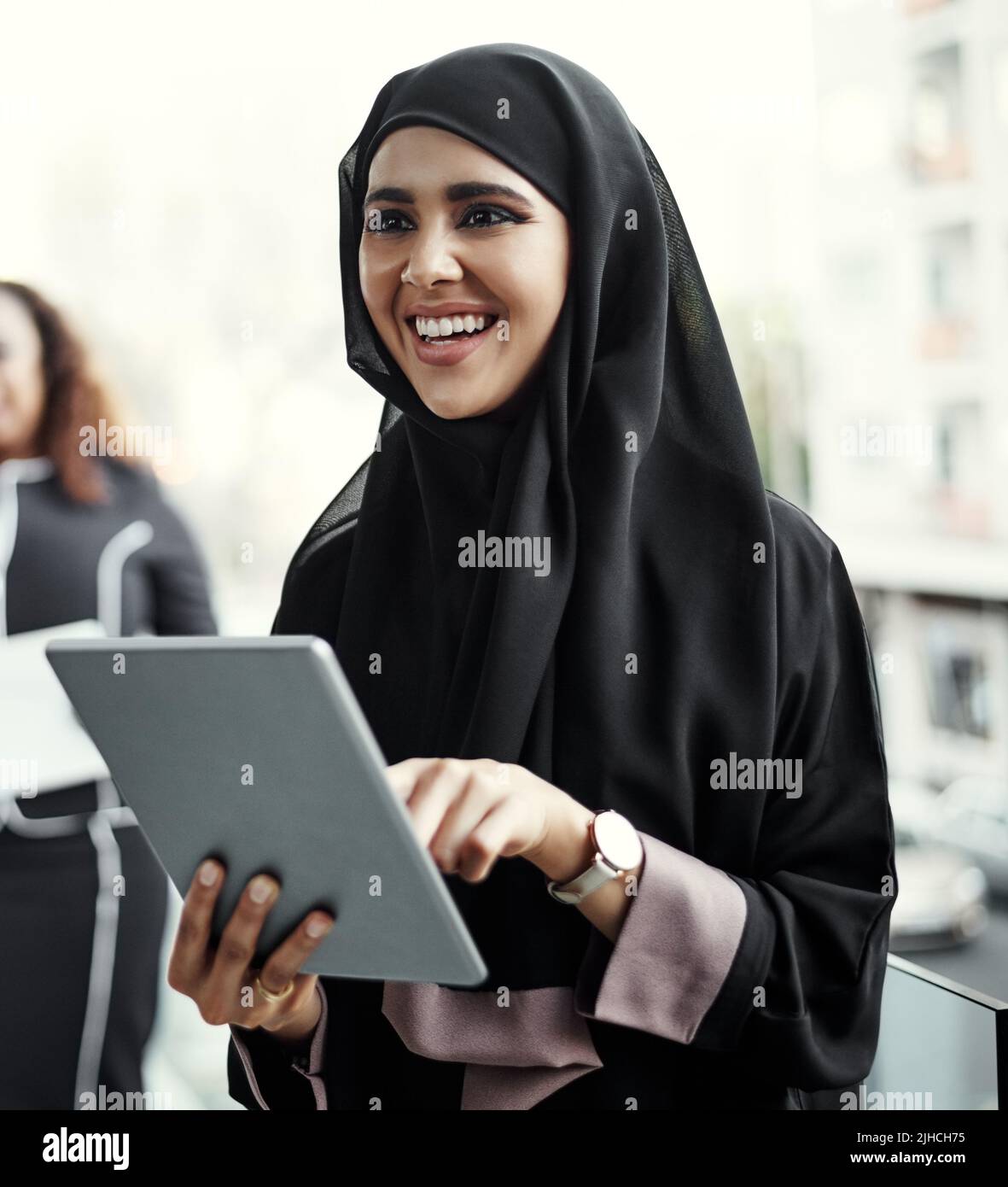 She enjoys working wirelessly. an attractive young businesswoman dressed in Islamic traditional clothing using a tablet on her office balcony. Stock Photo