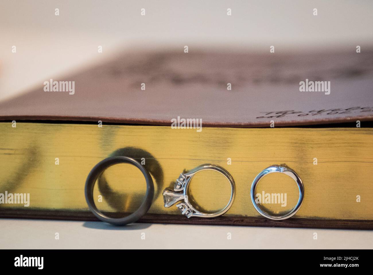 A close-up shot of rings leaning on a Bible with golden paper edges ...