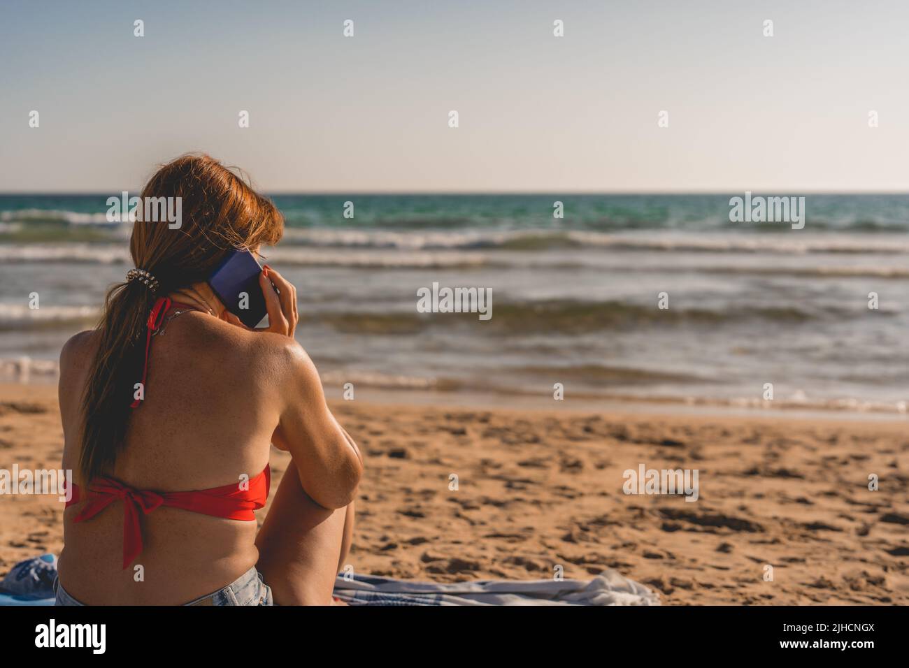 woman talking on her cell phone while sitting on the beach Stock Photo
