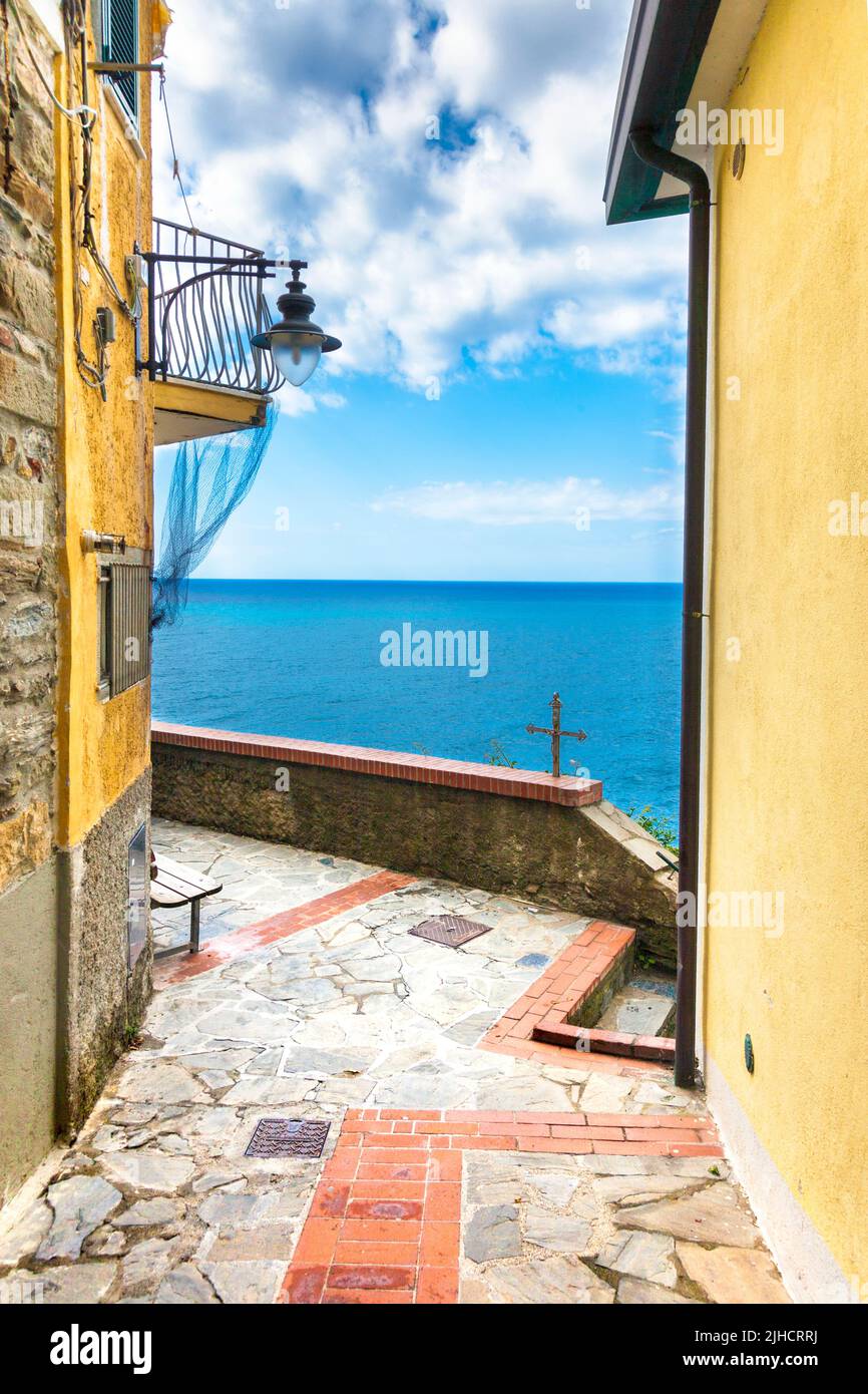A narrow street with yellow buildings overlooking the sea in Manarola, Cinque Terre, Italy Stock Photo