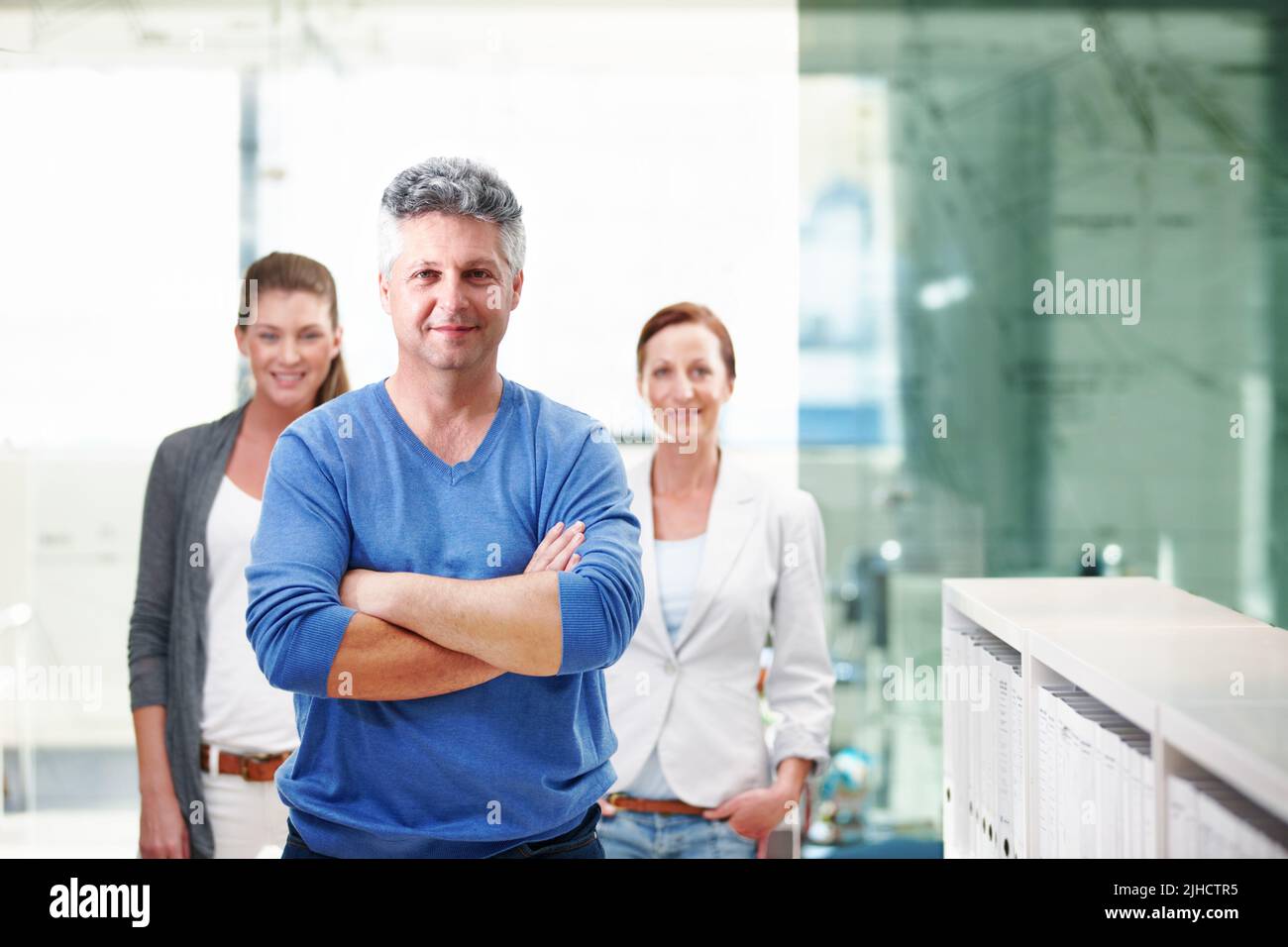 Hes got a wealth of experience. An mature businessman standing confidently with his co-workers behind him. Stock Photo