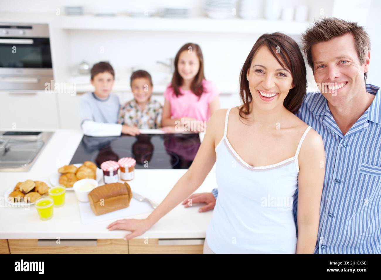 Keeping our family healthy, body and mind. A blissful couple standing alongside a wholesome breakfast with their children blurred in the background. Stock Photo