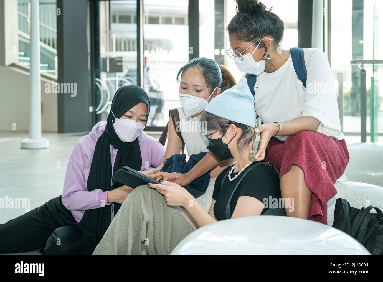 Group of young multi-ethnic Asian women with face mask on looking at a tablet together. Digital lifestyle concept. Stock Photo
