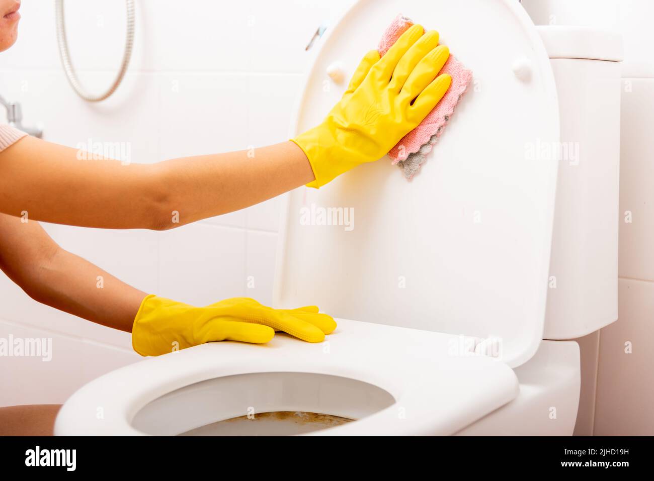 Hands of Asian woman cleaning toilet seat by pink cloth wipe restroom at house, female wearing