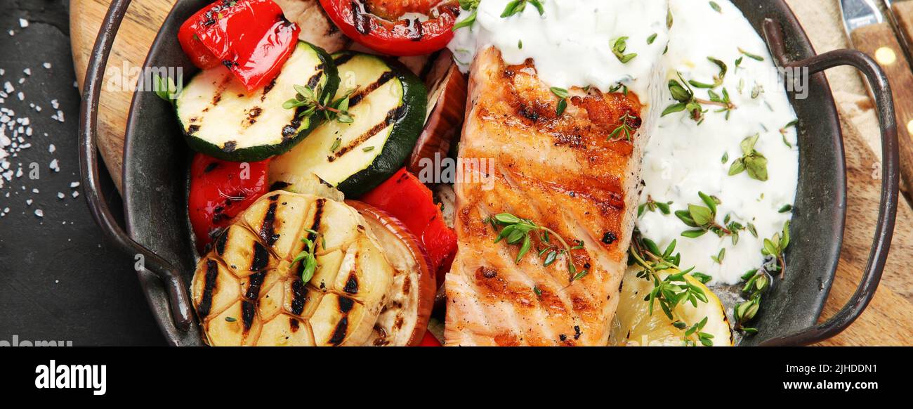 Salmon steak with vegetables and white sauce on dark background ...
