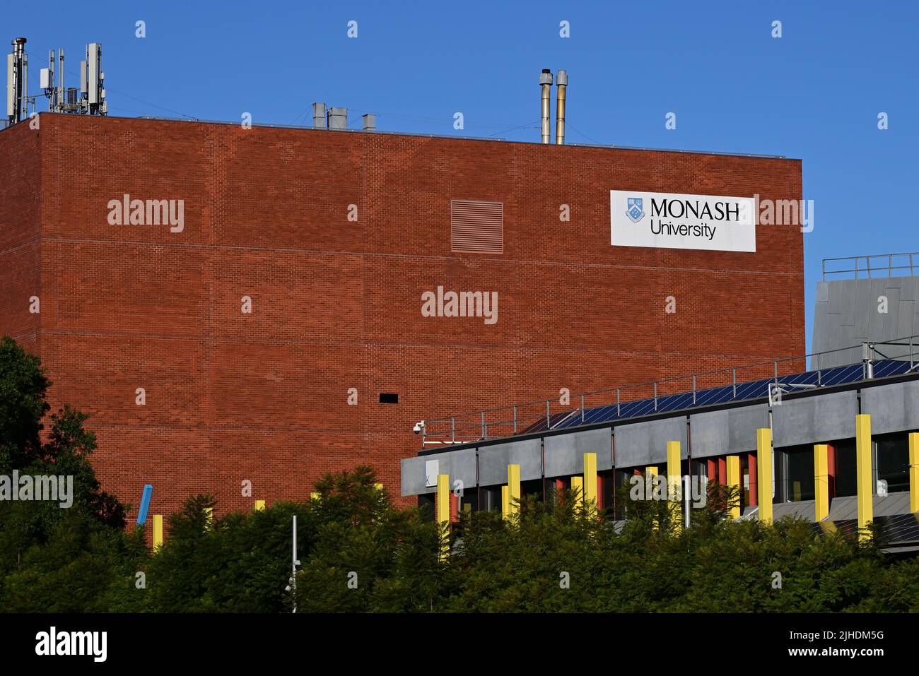 Building B, a red brick building featuring prominent signage, at Monash University's Caulfield Campus, with tree tops in the foreground Stock Photo