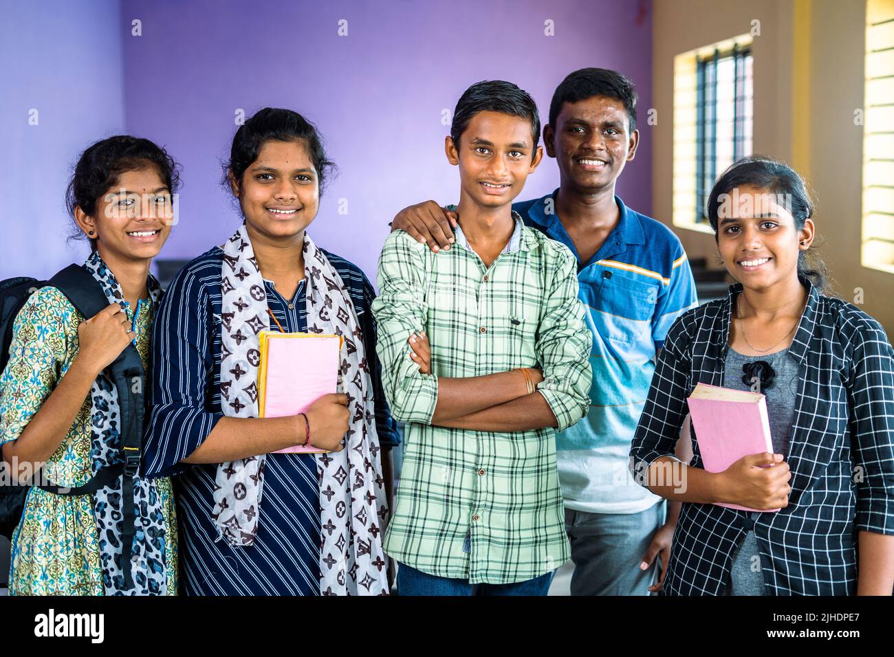 group of college students confidently standing with books and backpack at classroom by looking at camera - concept of education, friendship and Stock Photo