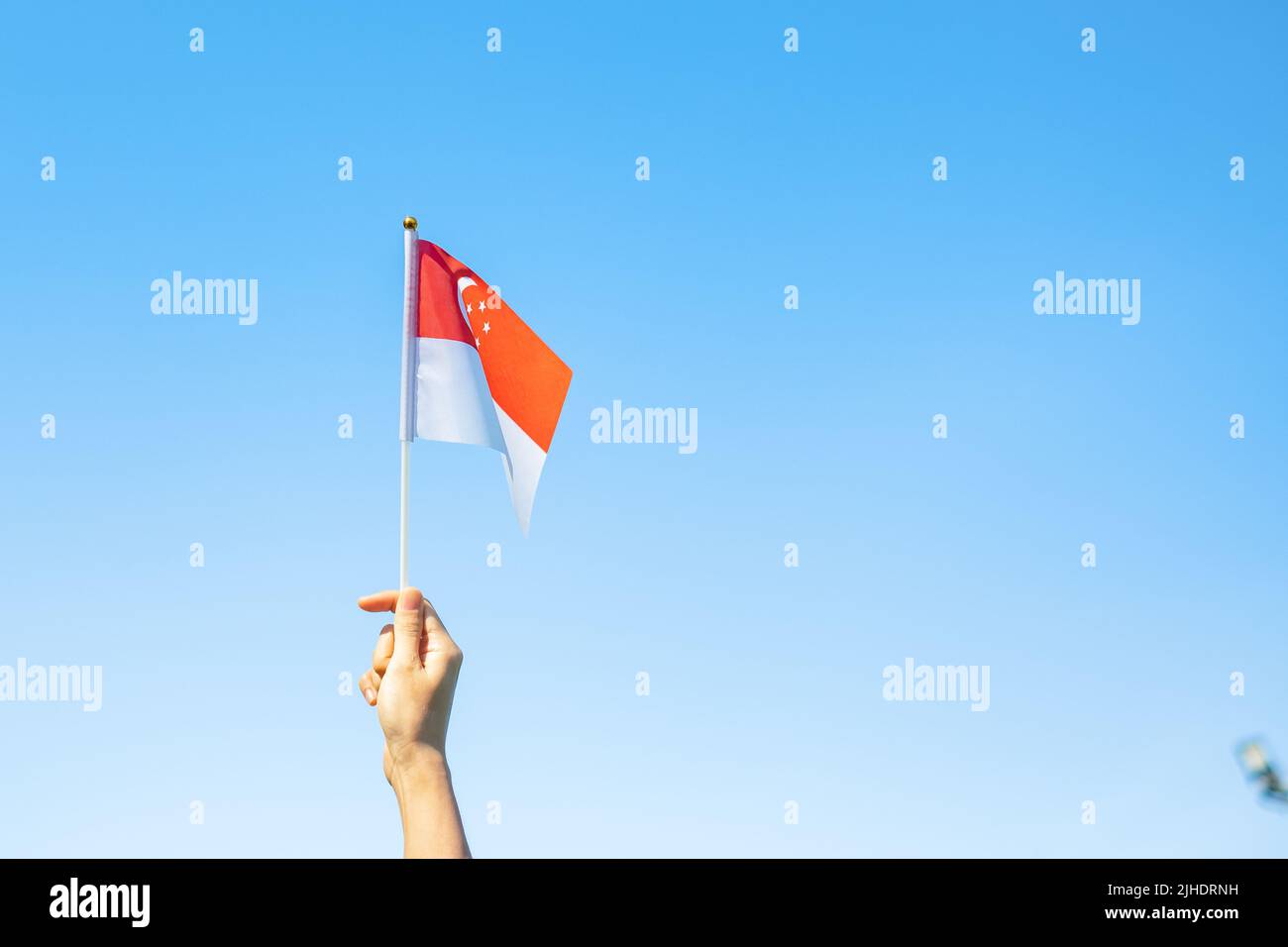 hand holding Singapore flag on blue sky background. Singapore National Day and happy celebration concepts Stock Photo