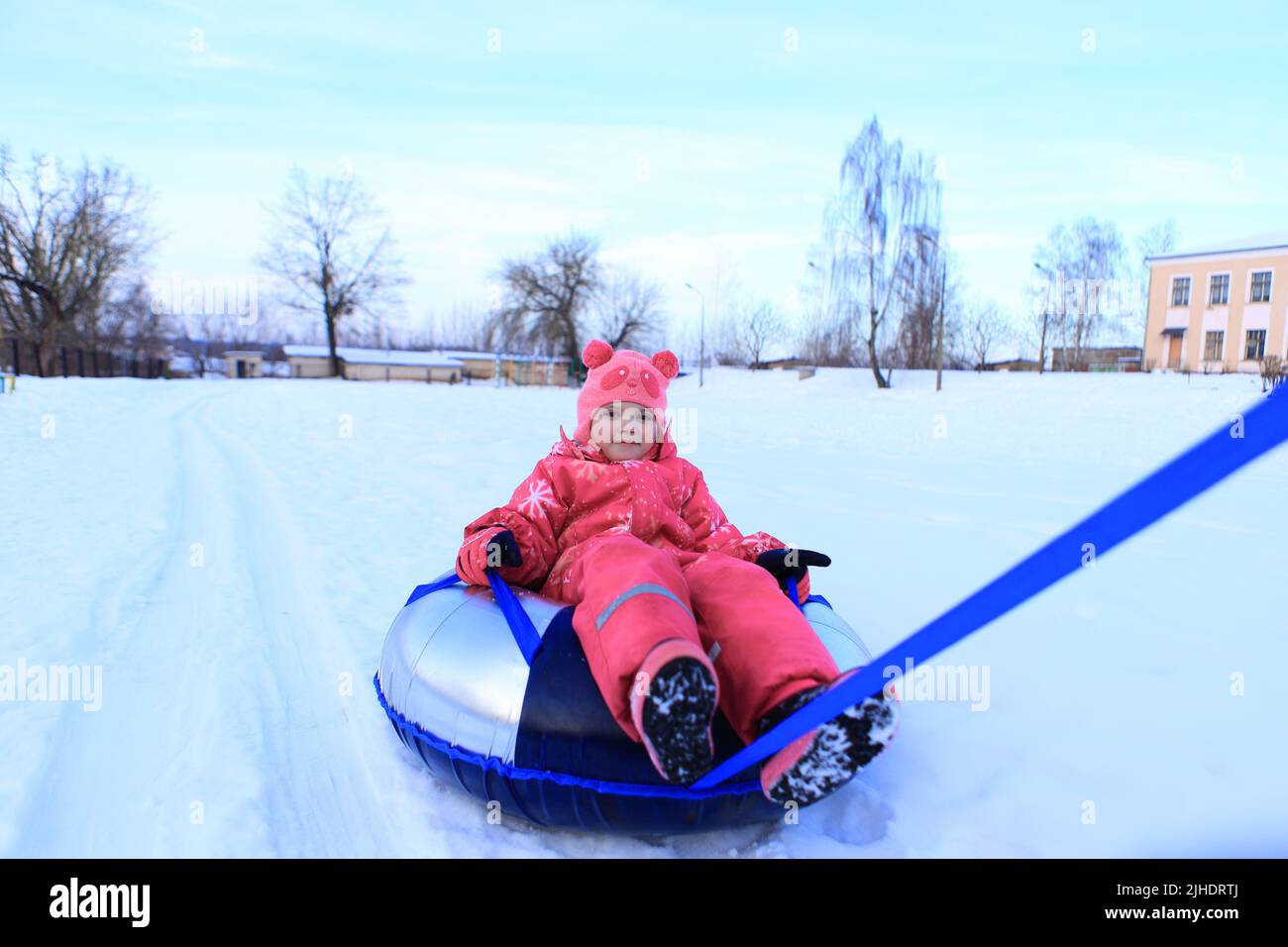 A girl in a winter overalls sits on a tubing. The child is sledding in the snow. Stock Photo