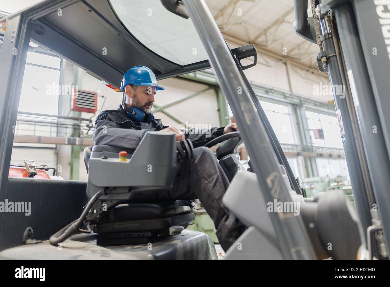 Happy mature man fork lift truck driver lifting pallet in storage