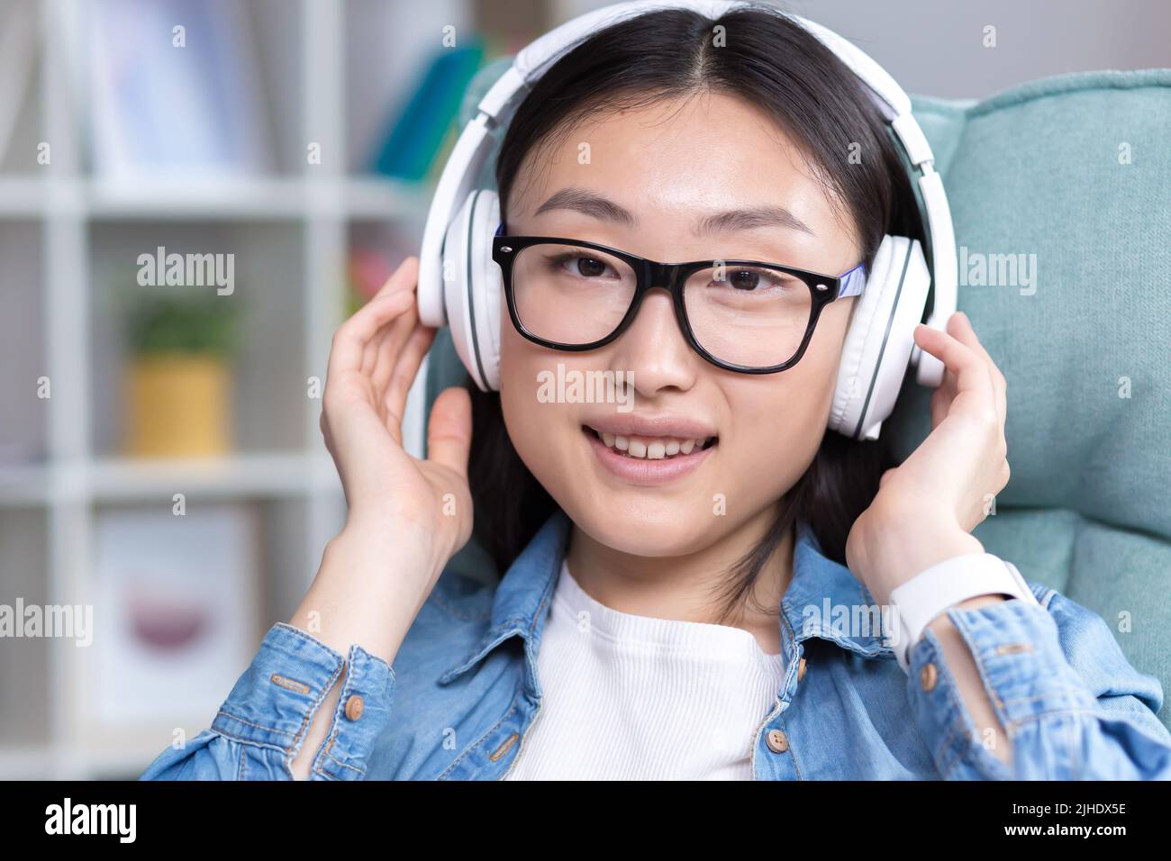 Young beautiful Asian woman listening to music in headphones, closing ...