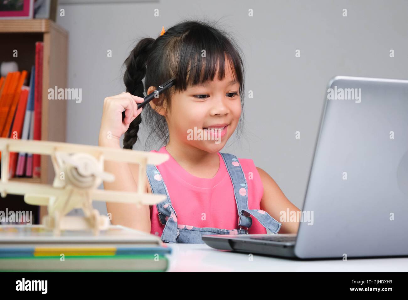 Smiling little Asian girl studying online having video call distant class with teacher using laptop. Happy girl learning English online with laptop at Stock Photo