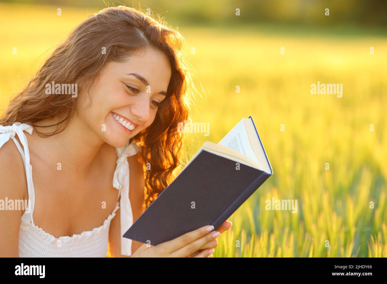 Happy woman reading a book smiling in a wheat field at sunset Stock Photo