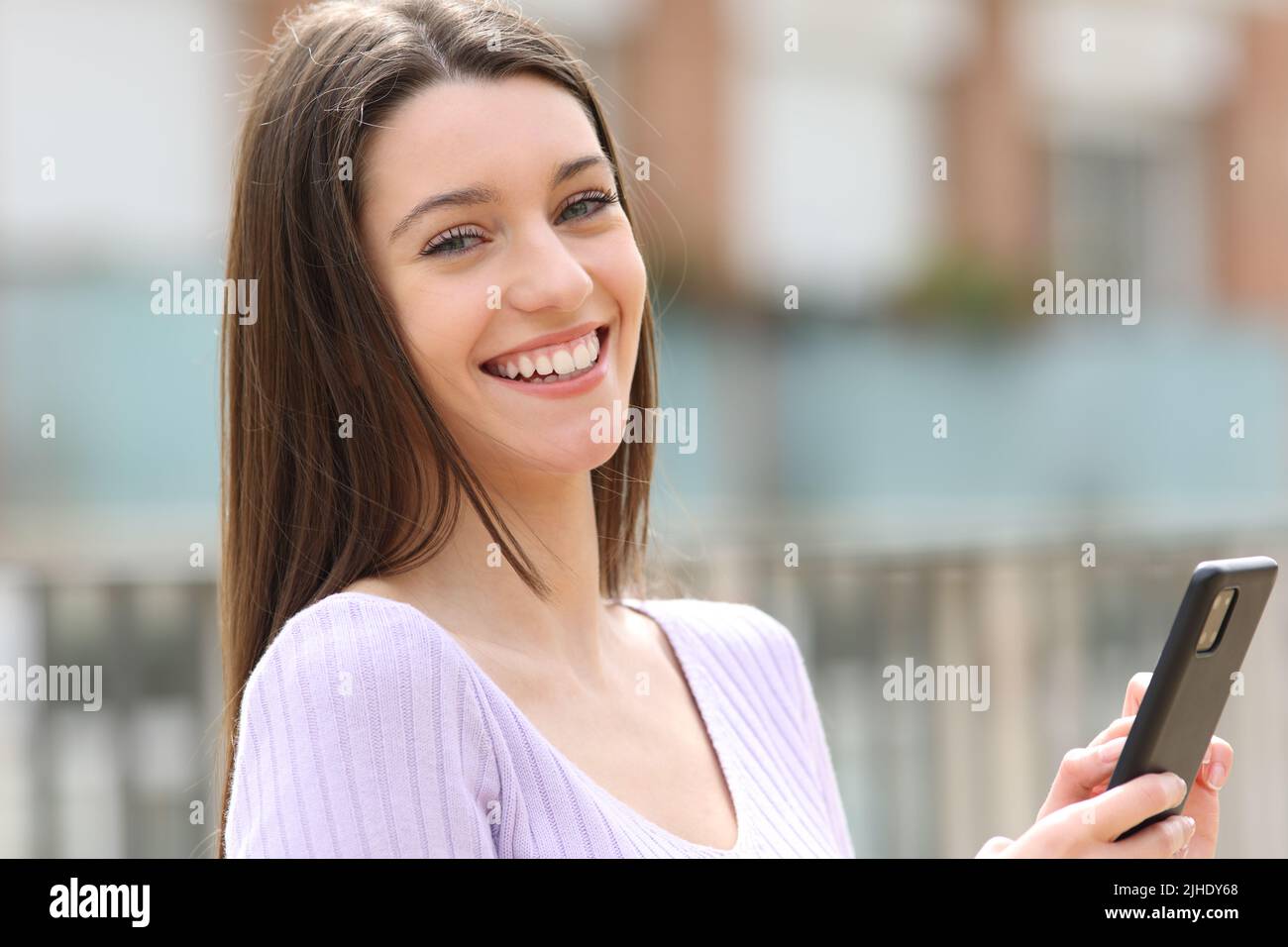 Portrait of a happy teen holding smart phone looking at camera in the street Stock Photo