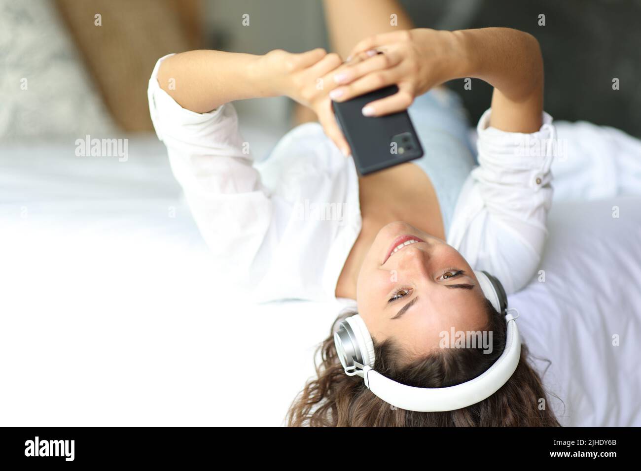 Happy woman listening to music wearing headphones on a bed Stock Photo