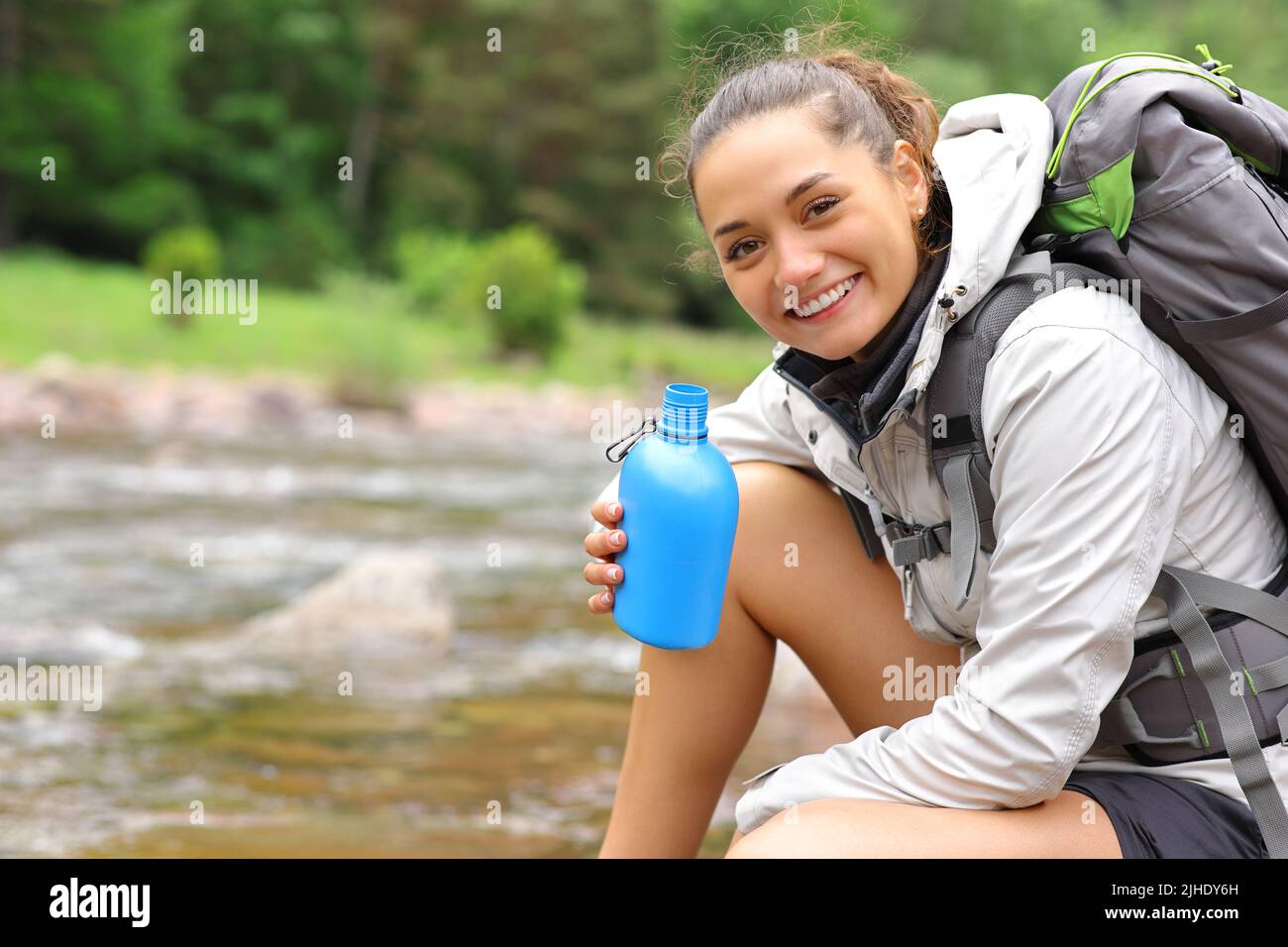 Happy hiker holding canteen looks at you in a riverside in the mountain Stock Photo