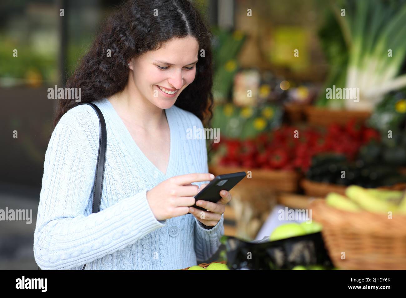 Customer using smart phone standing in a greengrocery Stock Photo