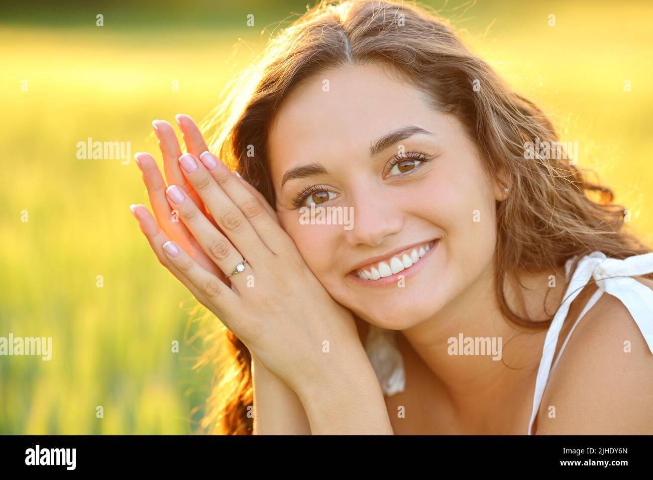 Engaged woman posing smiling looking at you showing ring in a field at sunset Stock Photo