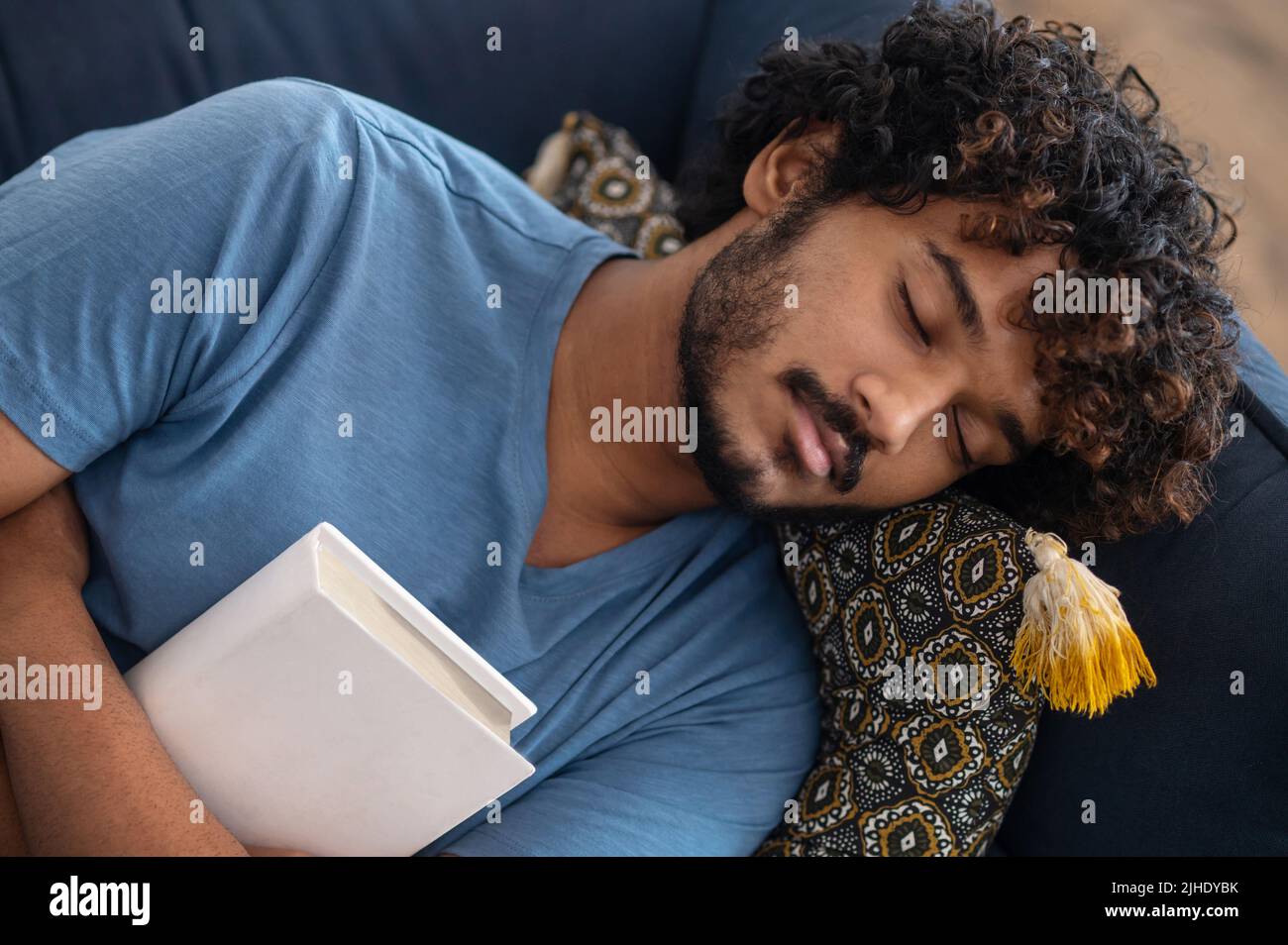 Young man sleeping on the sofa with a book in hands Stock Photo