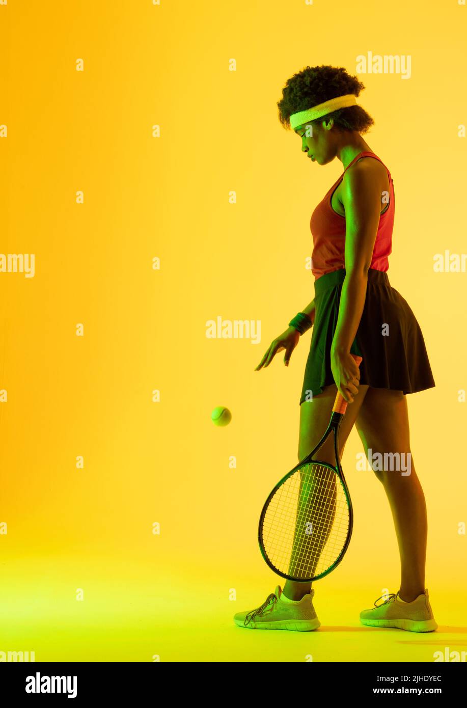 Vertical image of african american female tennis player in yellow lighting Stock Photo