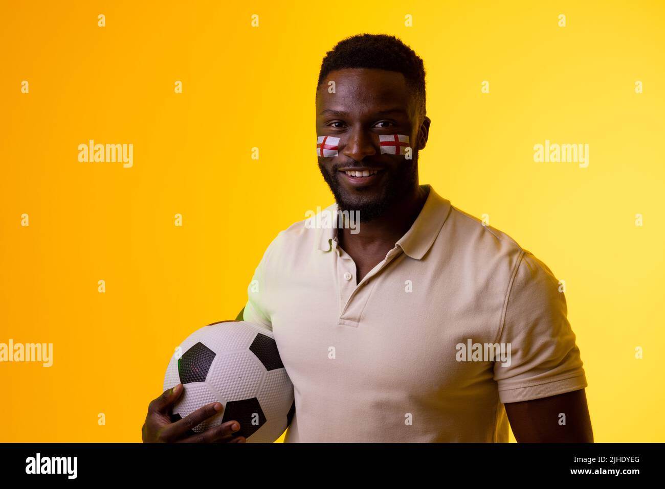 Image of happy african american male soccer fan with flag of england in yellow lighting Stock Photo