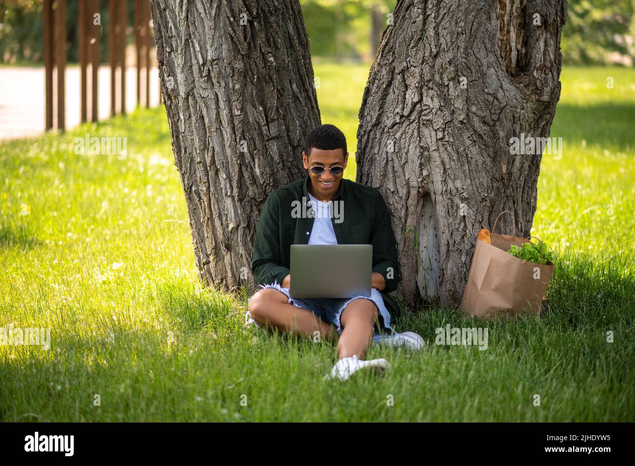Man smiling at laptop sitting under tree Stock Photo