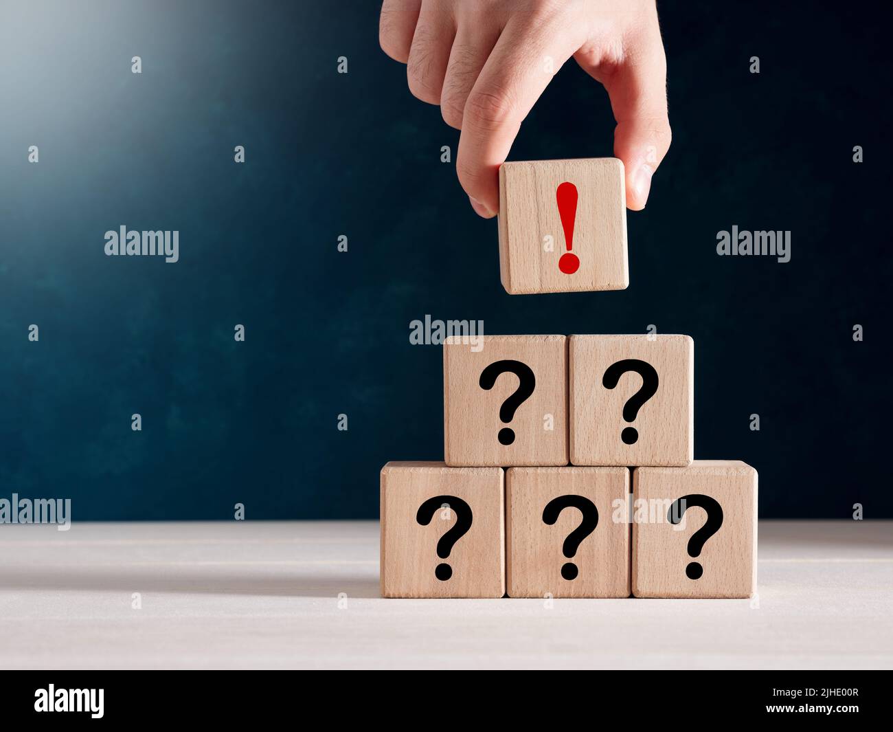 Concept of uncertainty, confusion and suspicion. Hand puts a wooden cube with exclamation mark at the top of stacked cubes with question mark. Stock Photo