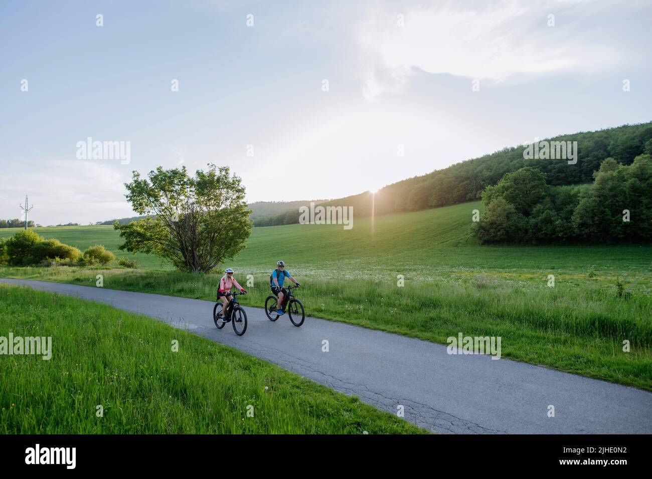 Active senior couple riding electric bicycles on trail at summer park, healthy lifestyle concept. Stock Photo