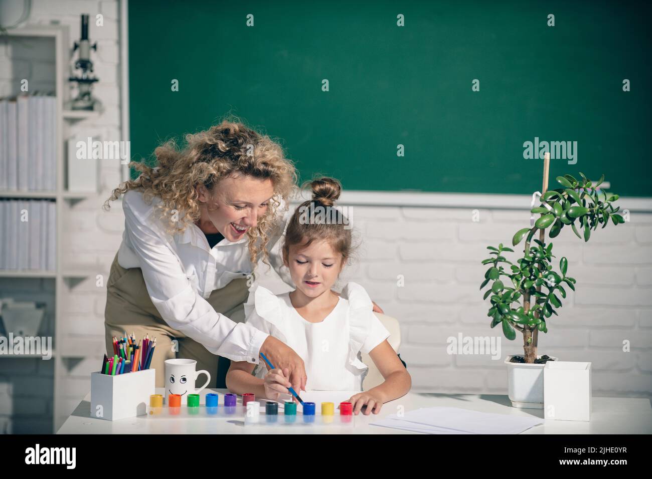 Kid drawing with teacher. Children from elementary school study at draw lesson. Pupil with