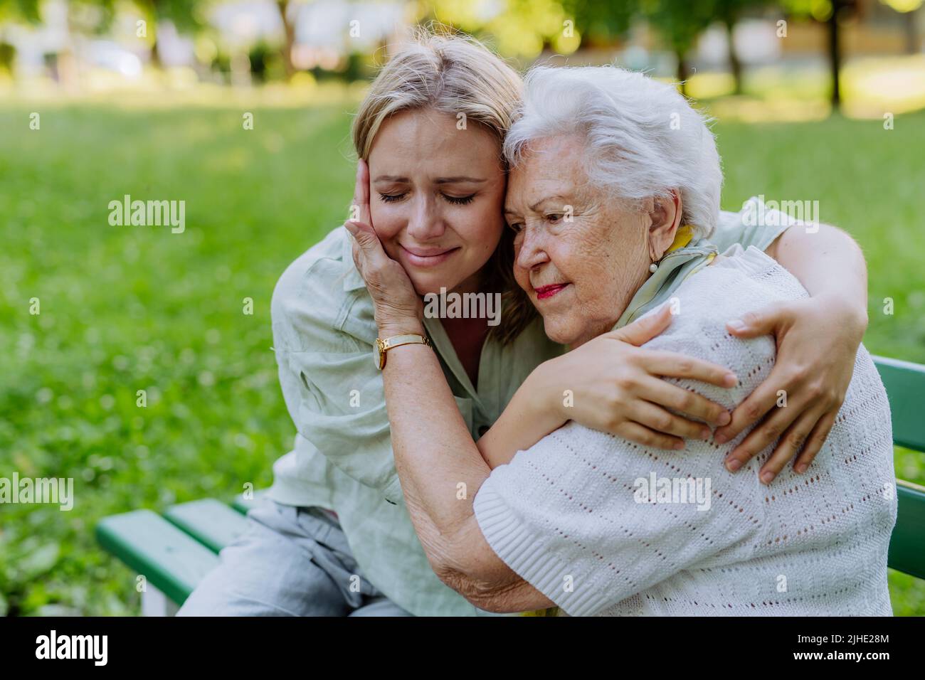 Worried senior grandmother comforting grown up granddaughter when sitting on bench in park, share problem with someone close concept Stock Photo