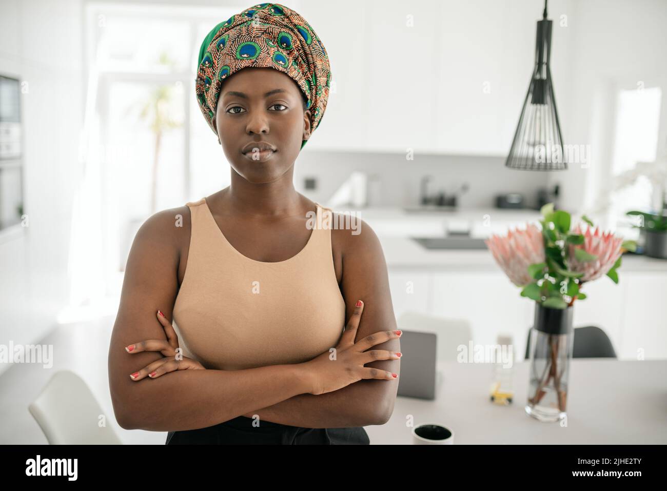 Portrait of a confident Black African woman with her arms crossed looking into the camera. Working from home and wearing a traditional headscarf Stock Photo