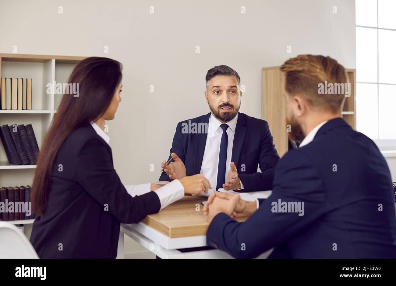 Business meeting in office of law firm of male lawyer and married couple of clients. Stock Photo