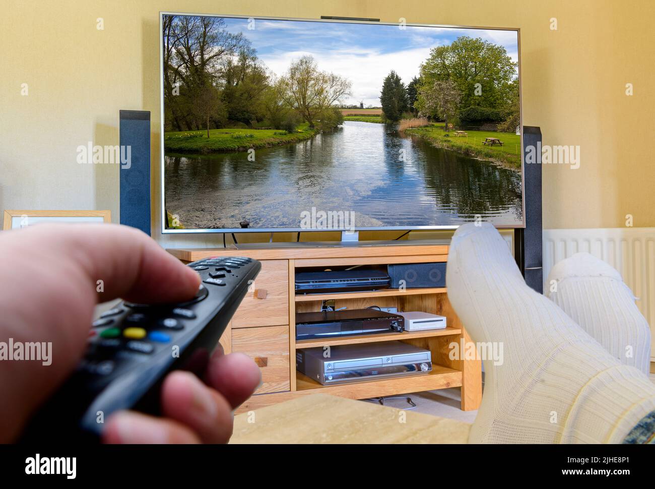 couch potato Man with feet up watching a large flat screen tv remote control in hand changing channels Stock Photo