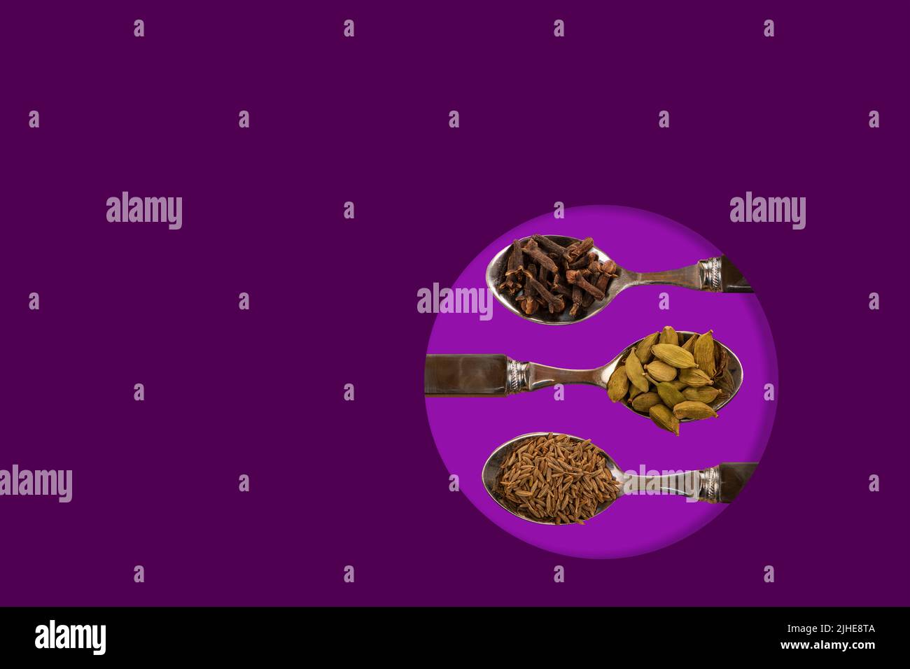 selection assorted indian spices cumin seeds cardamom cardamon pods cloves display on spoons on a colorful colourful purple background Stock Photo